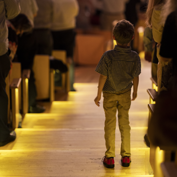 A child stands during a concert, looking at the stage. He is illuminated by the aisle lights.